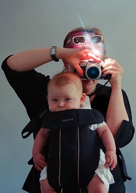 Woman with baby in sling filming selfie in mirror